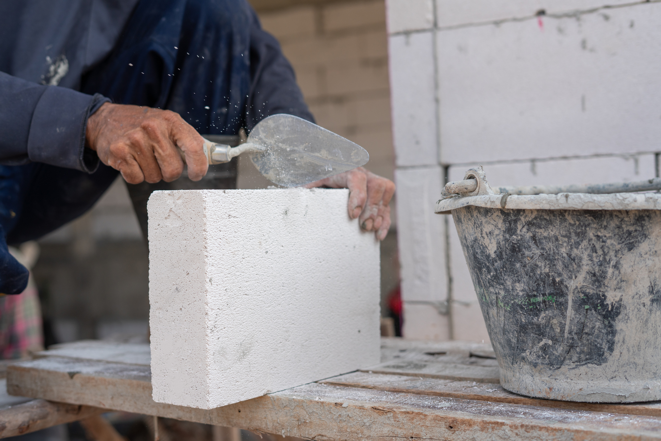 Skilled Mason Applying Mortar To Concrete Block At Construction Site